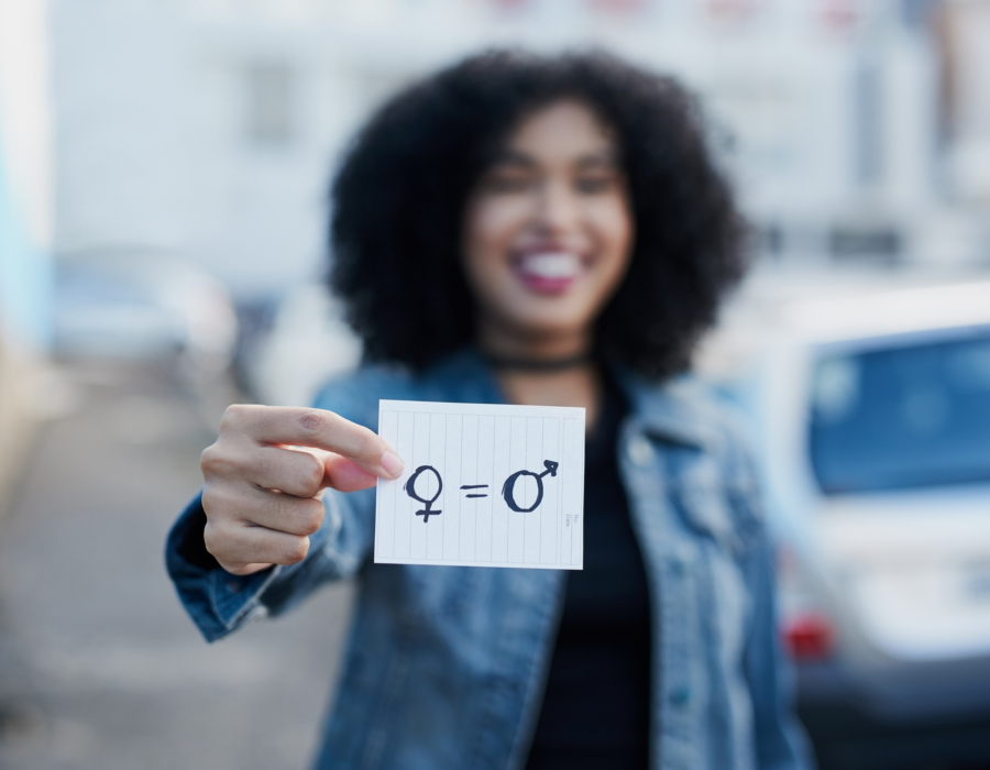 Out of focus woman holding a piece of paper with gender symbols and equals sign drawn on it.